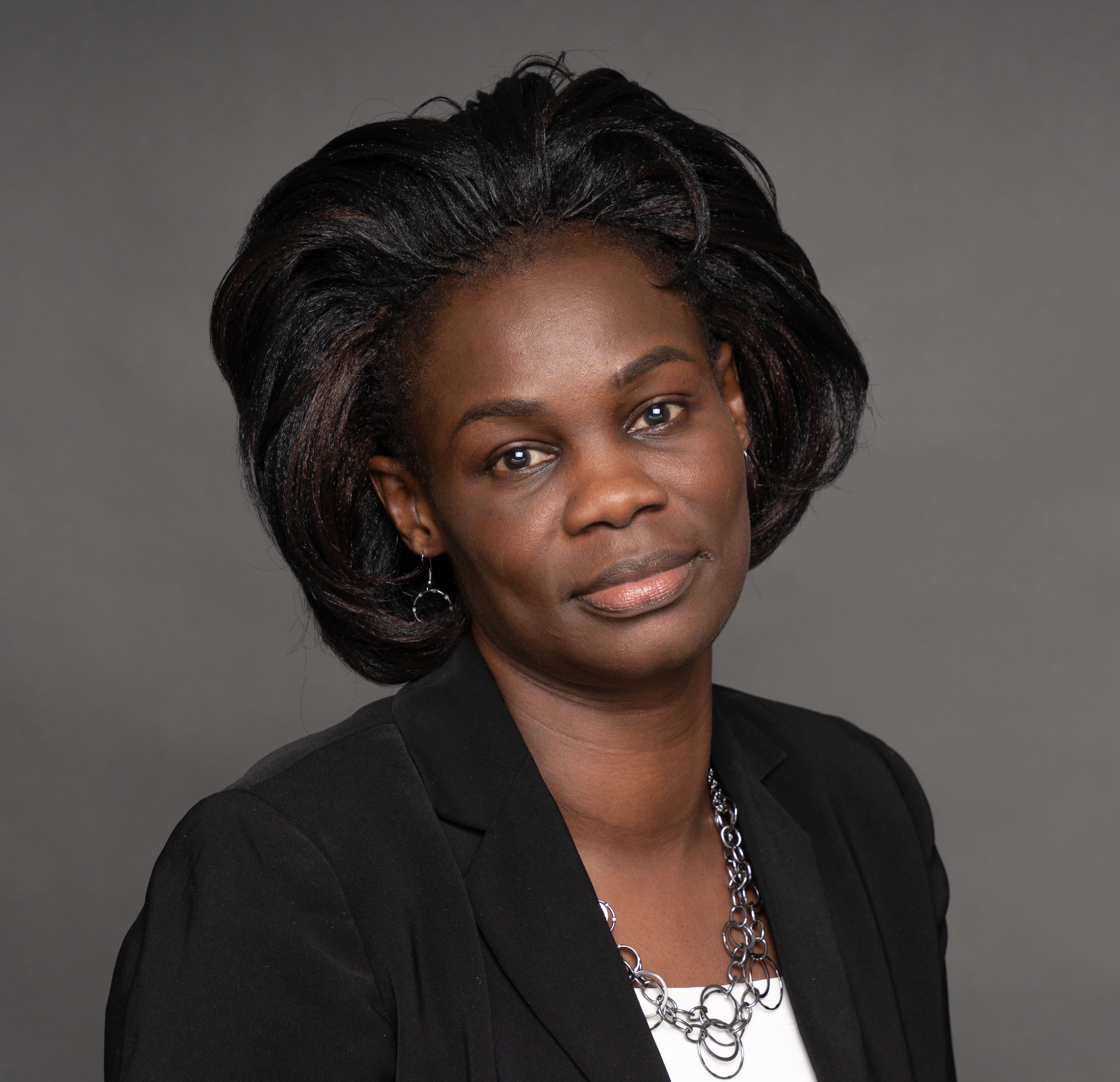 A woman in a dark suit in front of a grey background facing the camera.
