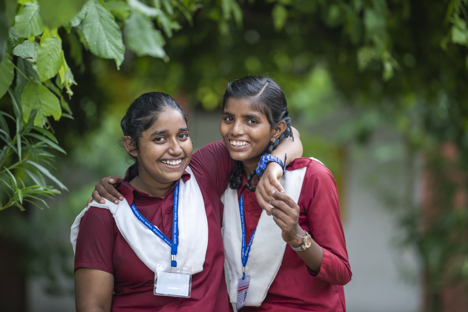 Ni Varanasi 2022 - Nutrition International Two girls in school uniforms laugh to the camera with their arm around their friend.