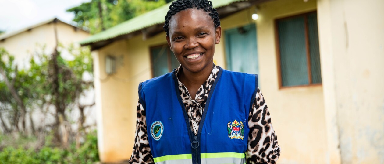 A woman wearing a blue community health volunteer vest smiles looking at the camera