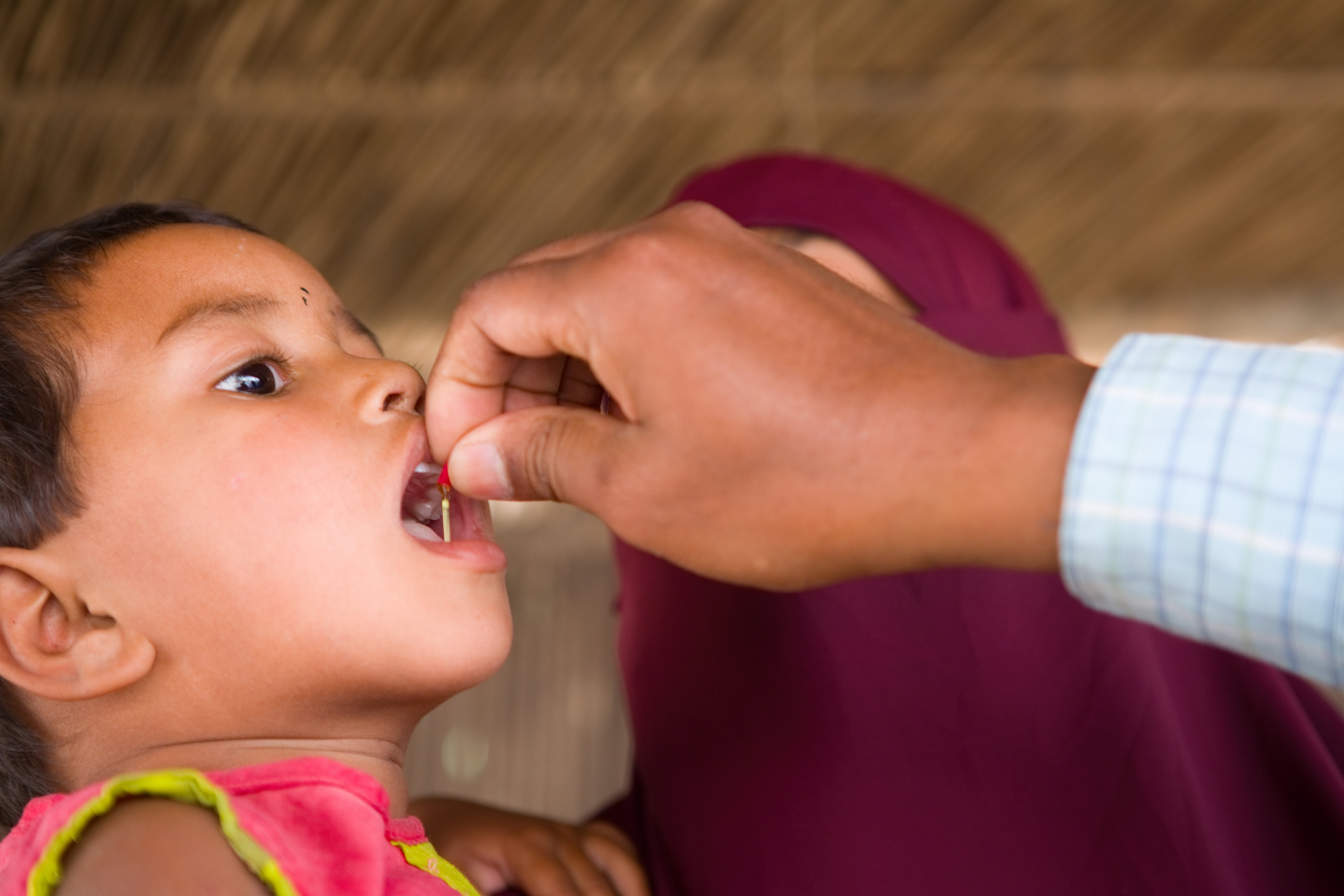 A child opens their mouth and receives a doplet from a capsule containing vitamin A supplementation.