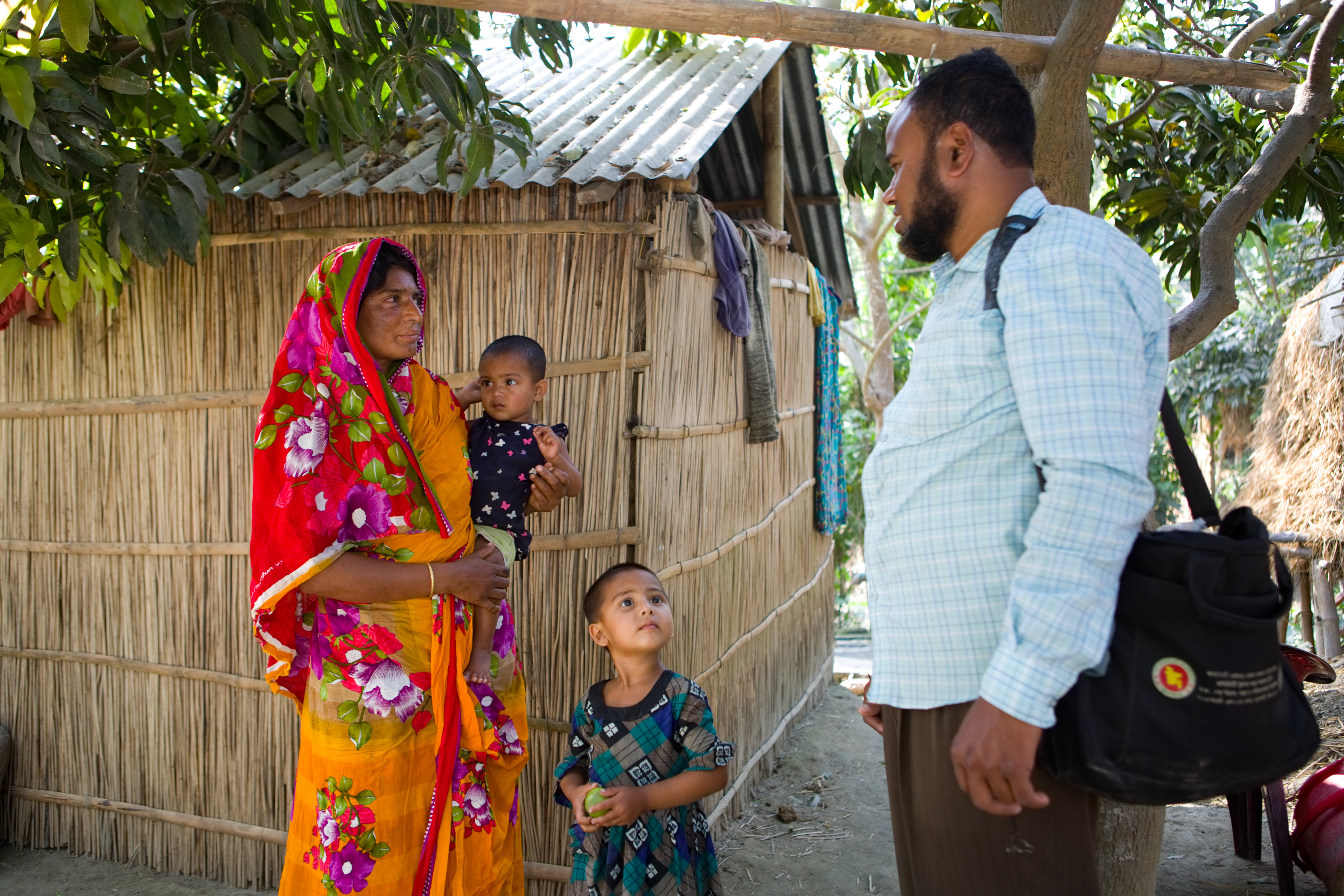 A  woman stands with two children speaking to a man. They are standing outside and have slight smiles on their faces.