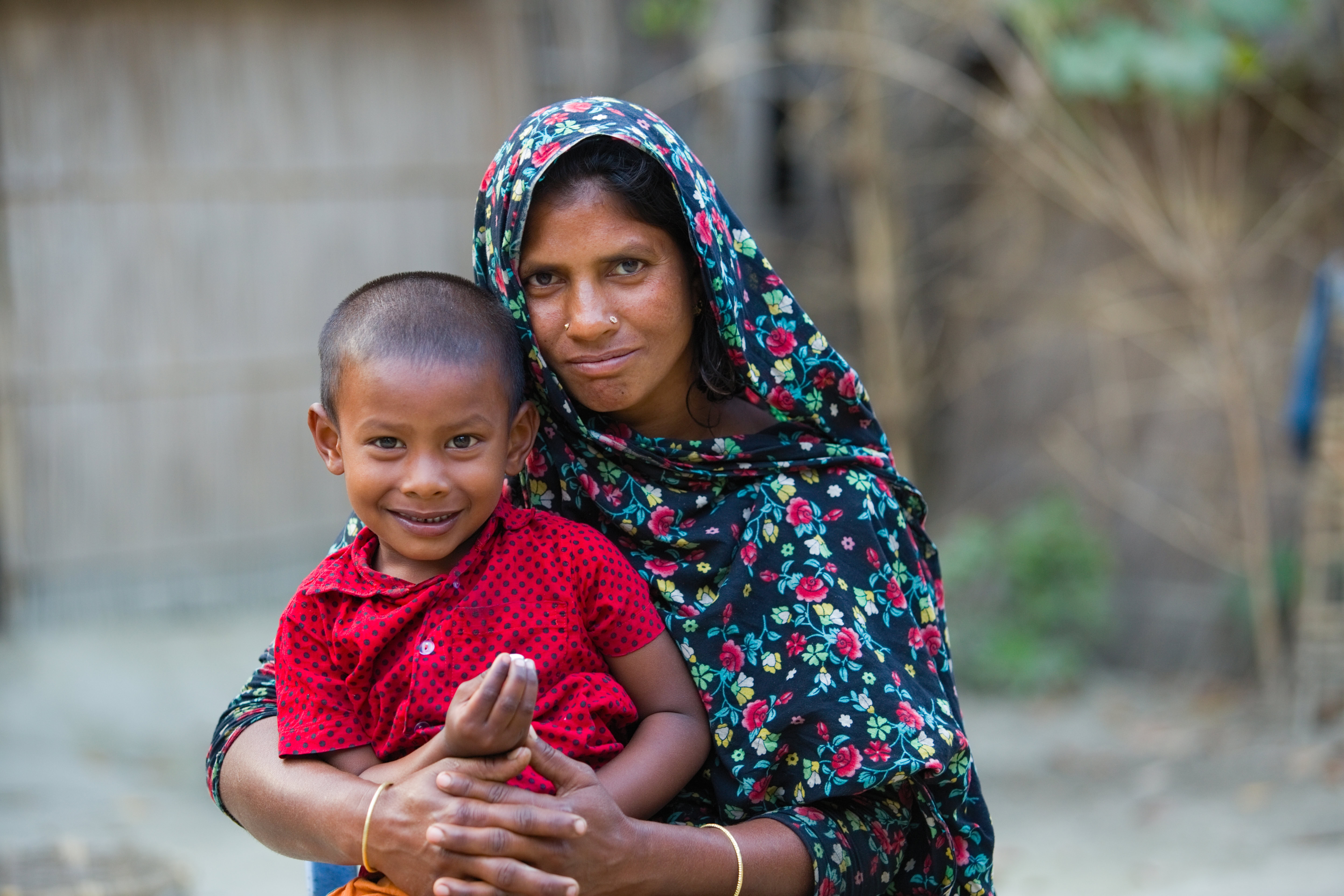 A little boy sits in his mothers lap. Both are looking at the camera and smiling.