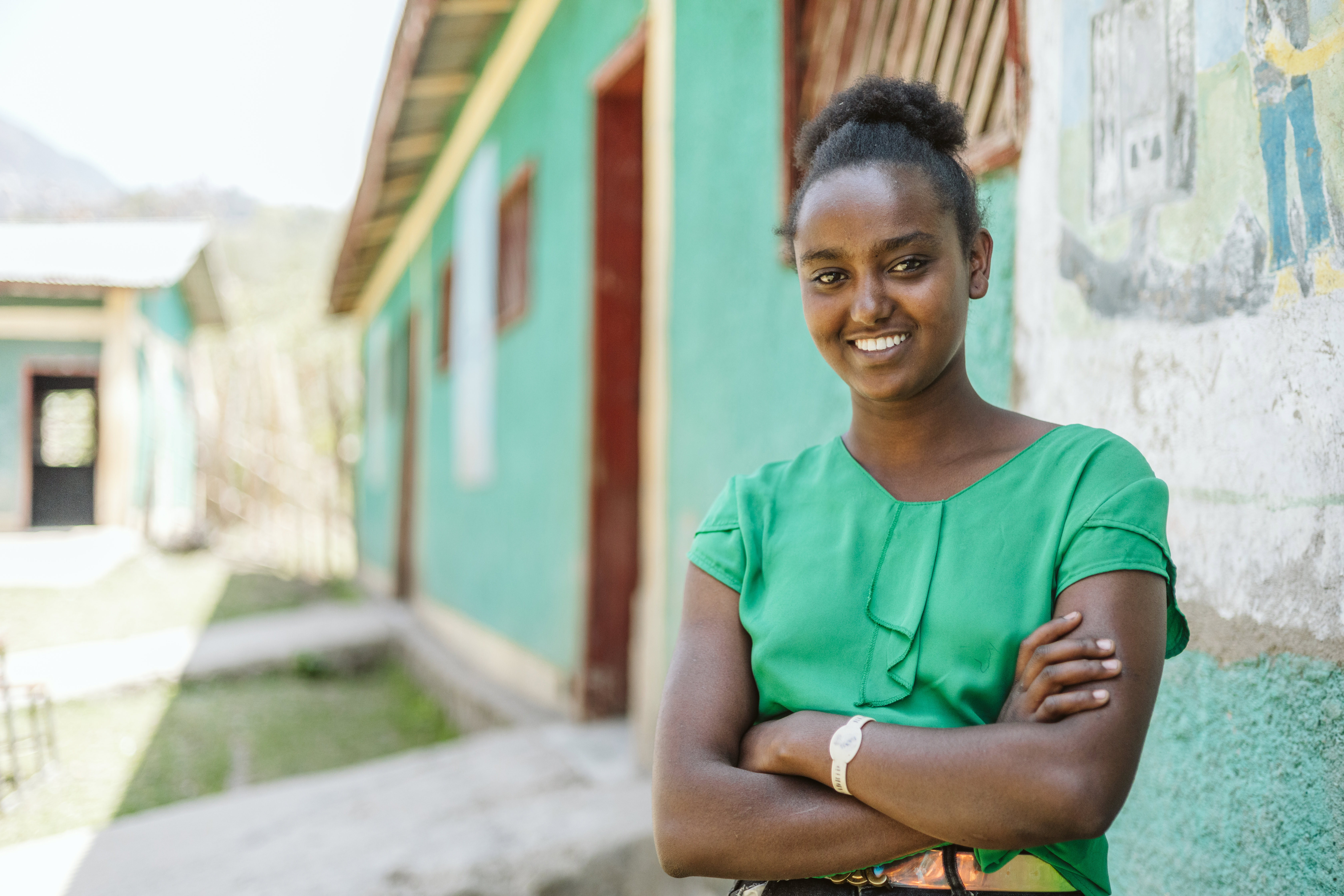 A gift stands in front of a building. She is smiling looking at the camera with her arms crossed in front of each.