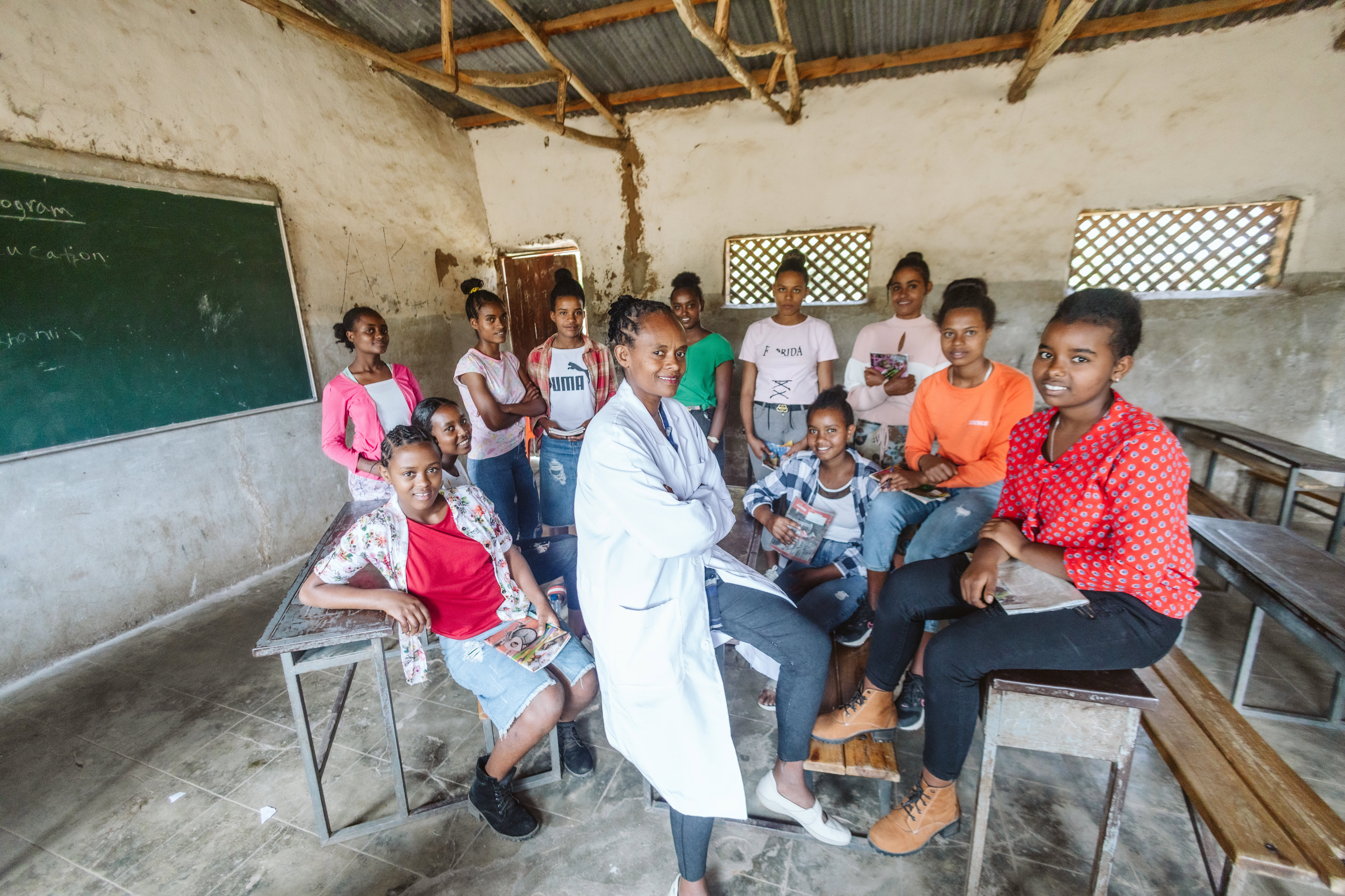 A group of female students and their teacher stands as a group. They are facing the camera and smiling.