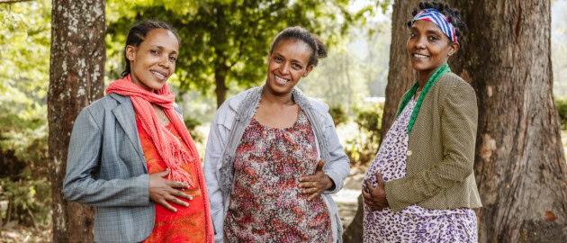 Three pregnant women stand outside smiling to the camera