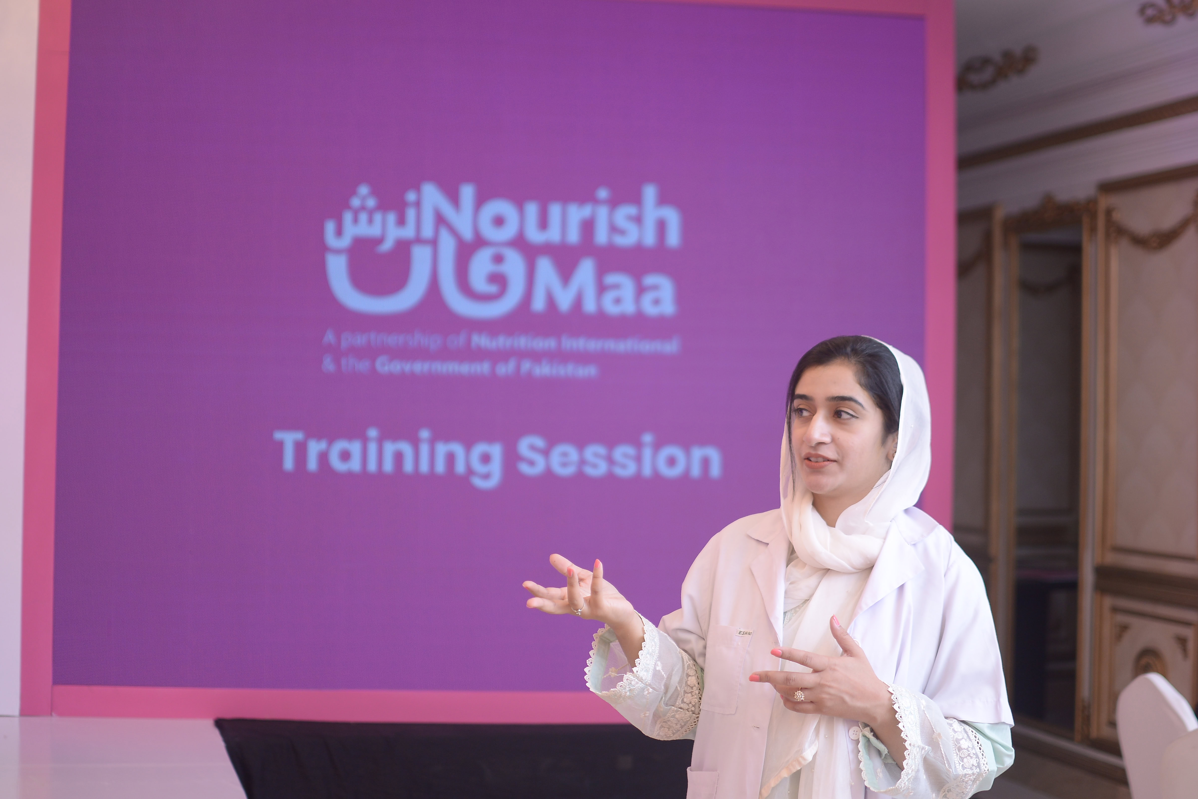 A woman speaking in front of a screen that says NourshMass