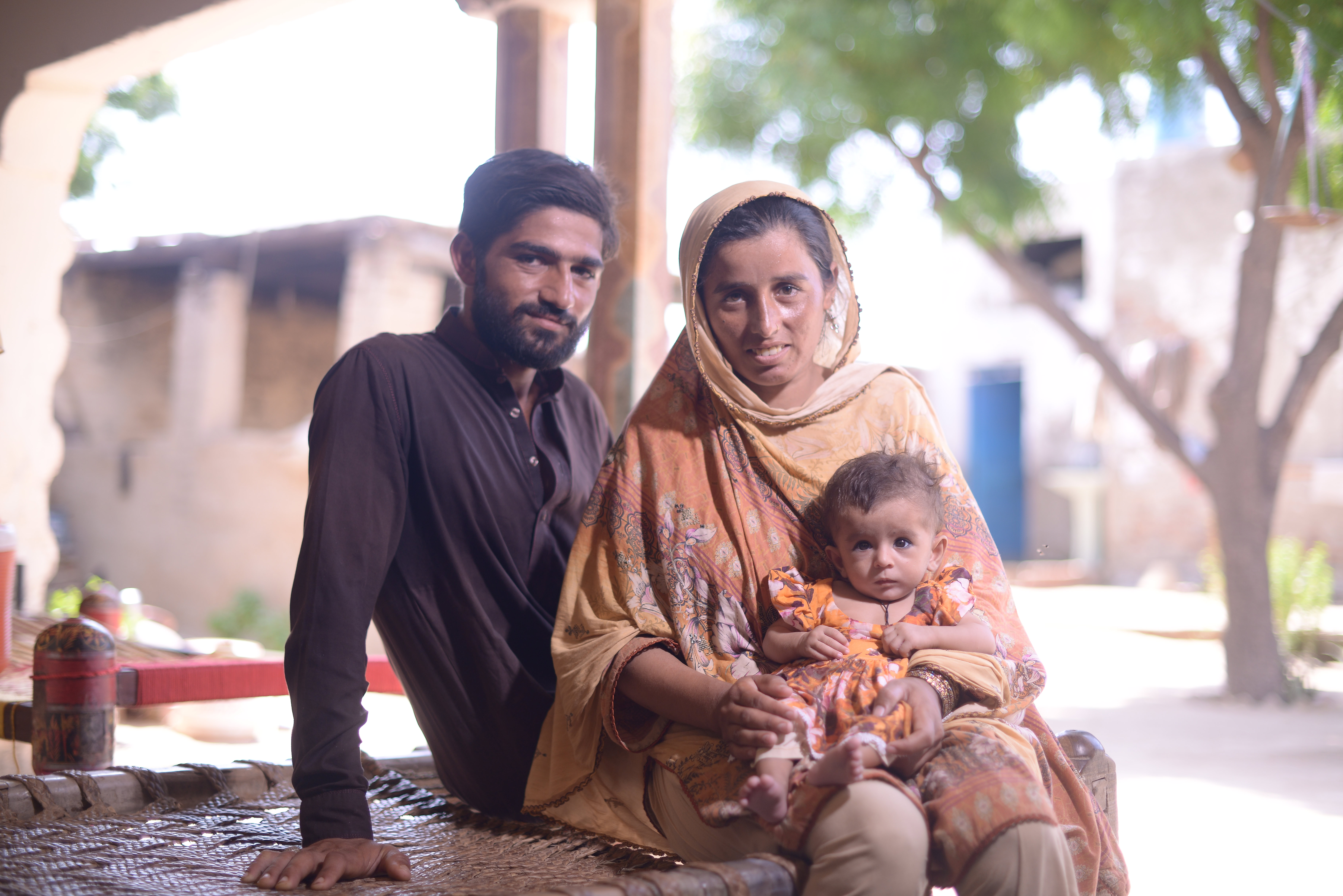 A couple smiles to the camera holding their baby on the mother's lap.