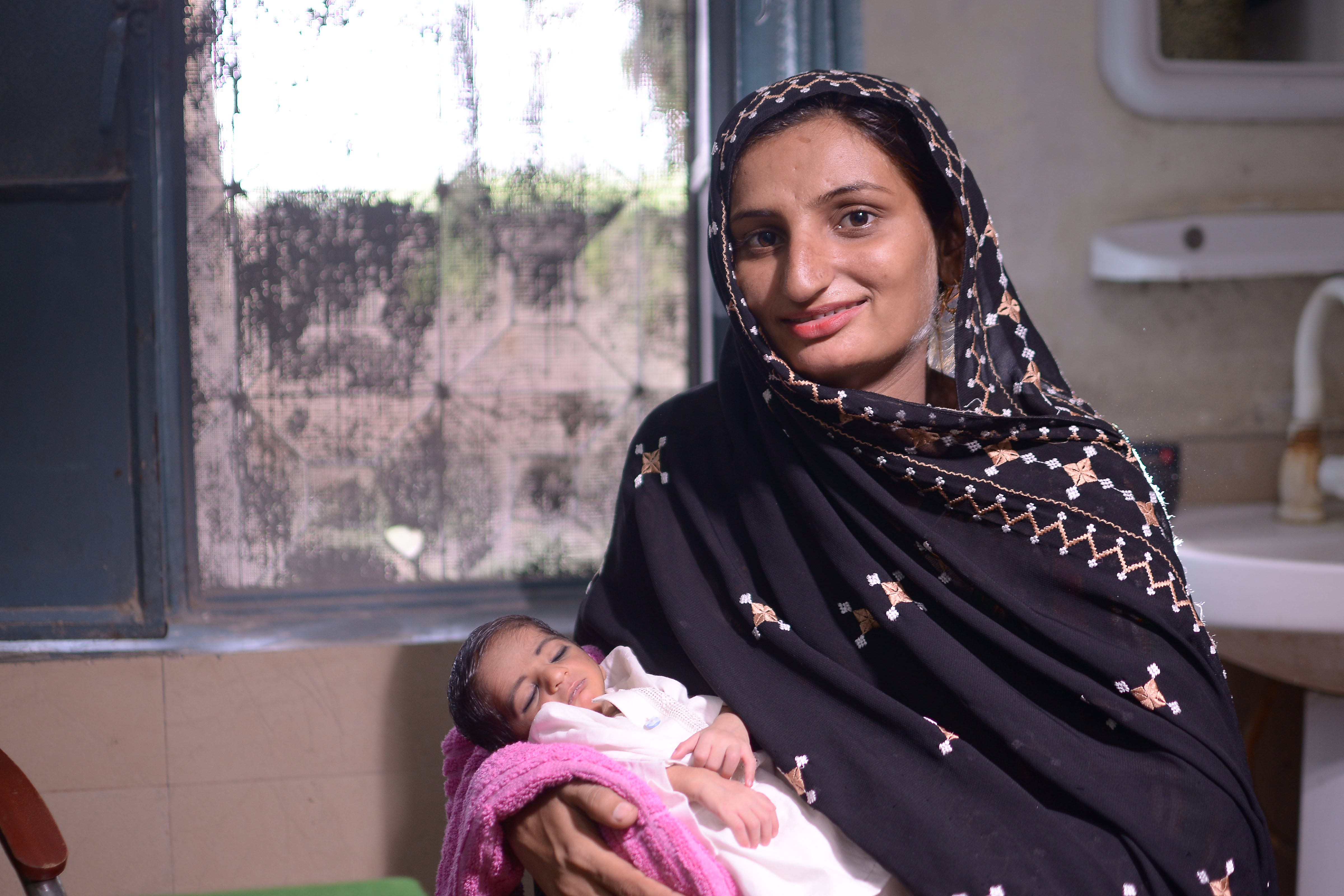 A mother holds her newborn and smiles to the camera.