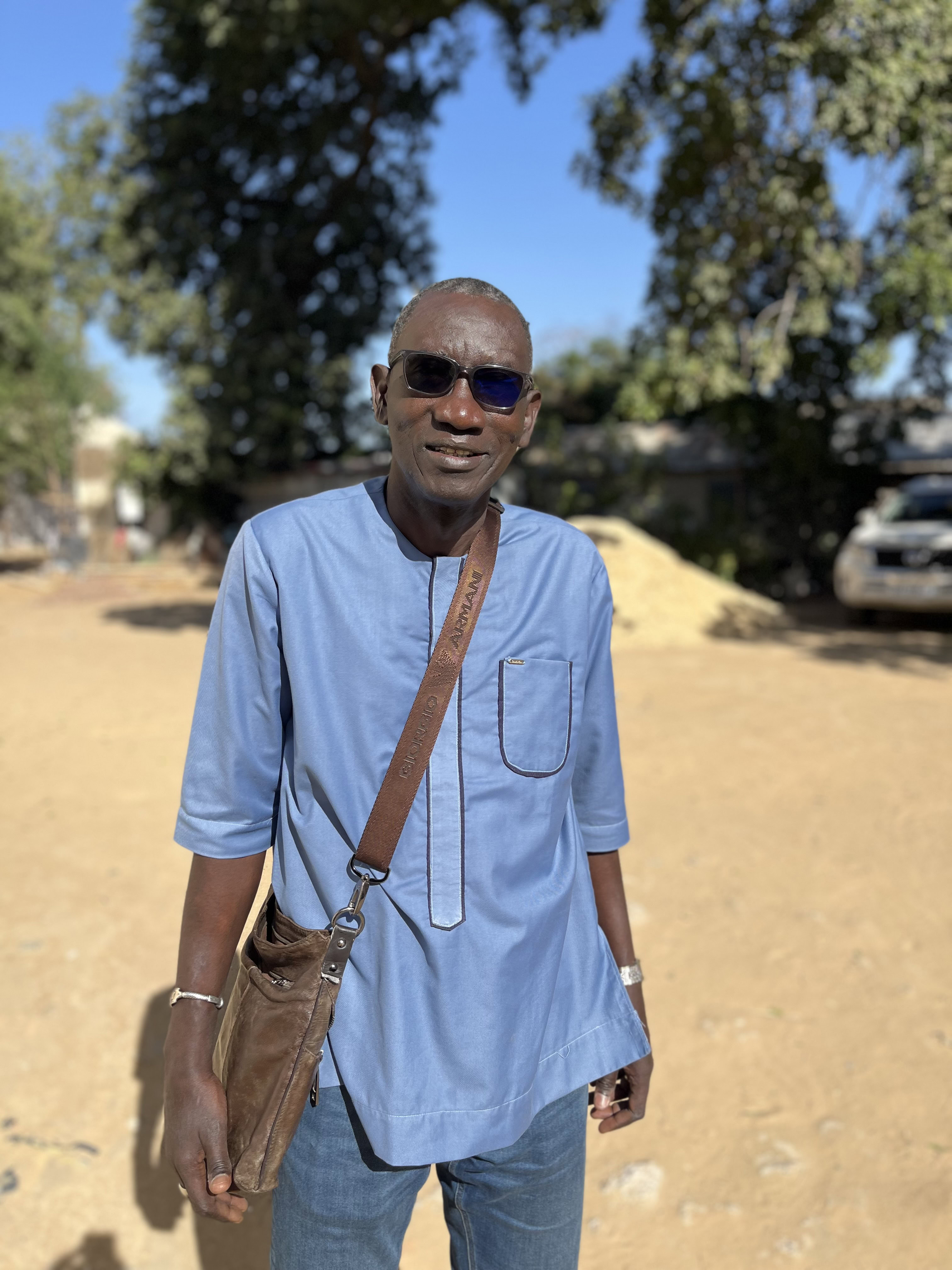 Ibrahima Ndao, prodject directo for VAS in Chad, stands outisde in a blue shirt smiling to camera.