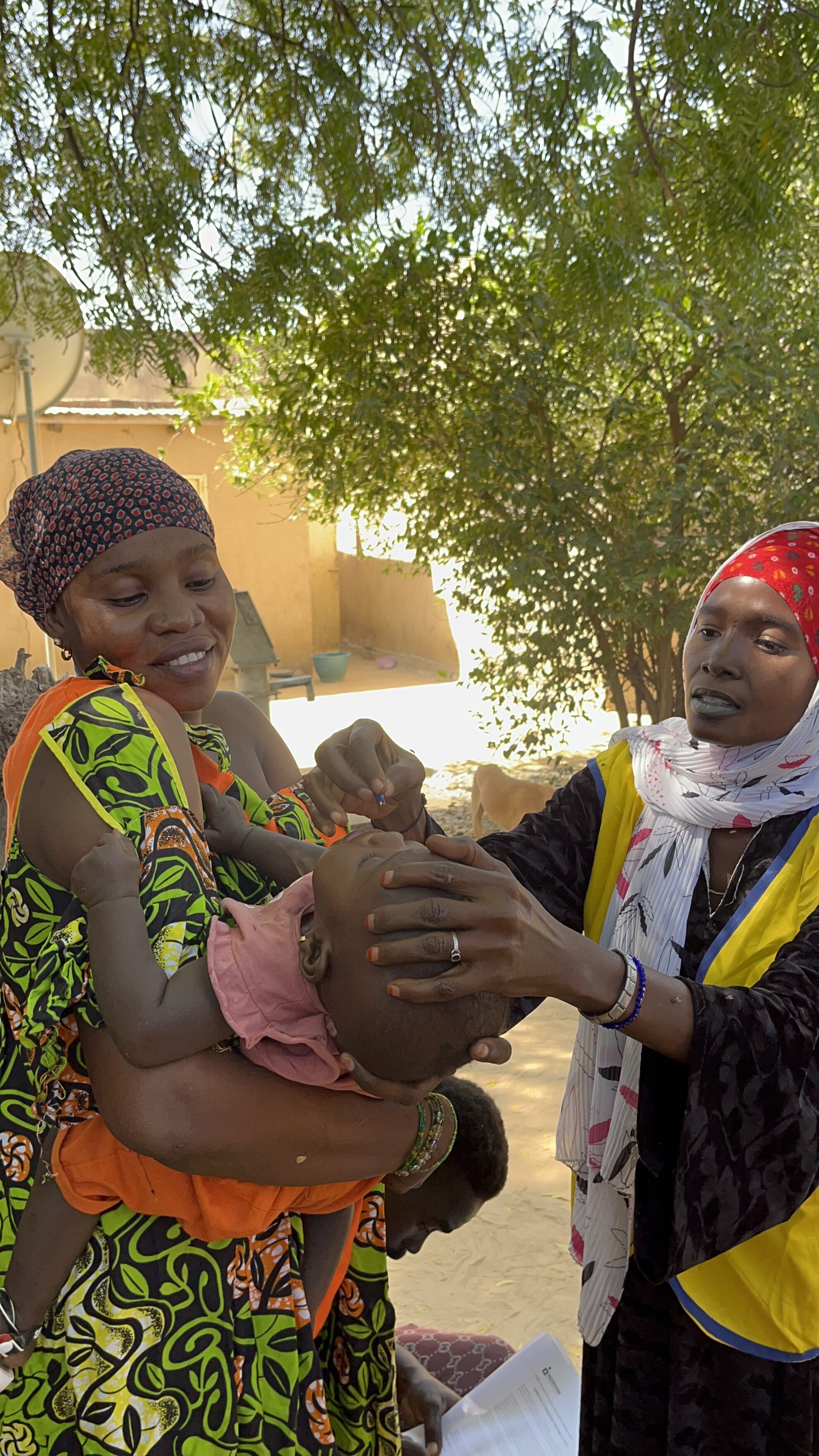 A woman administers vitamin A to a child who is being held by their mother.