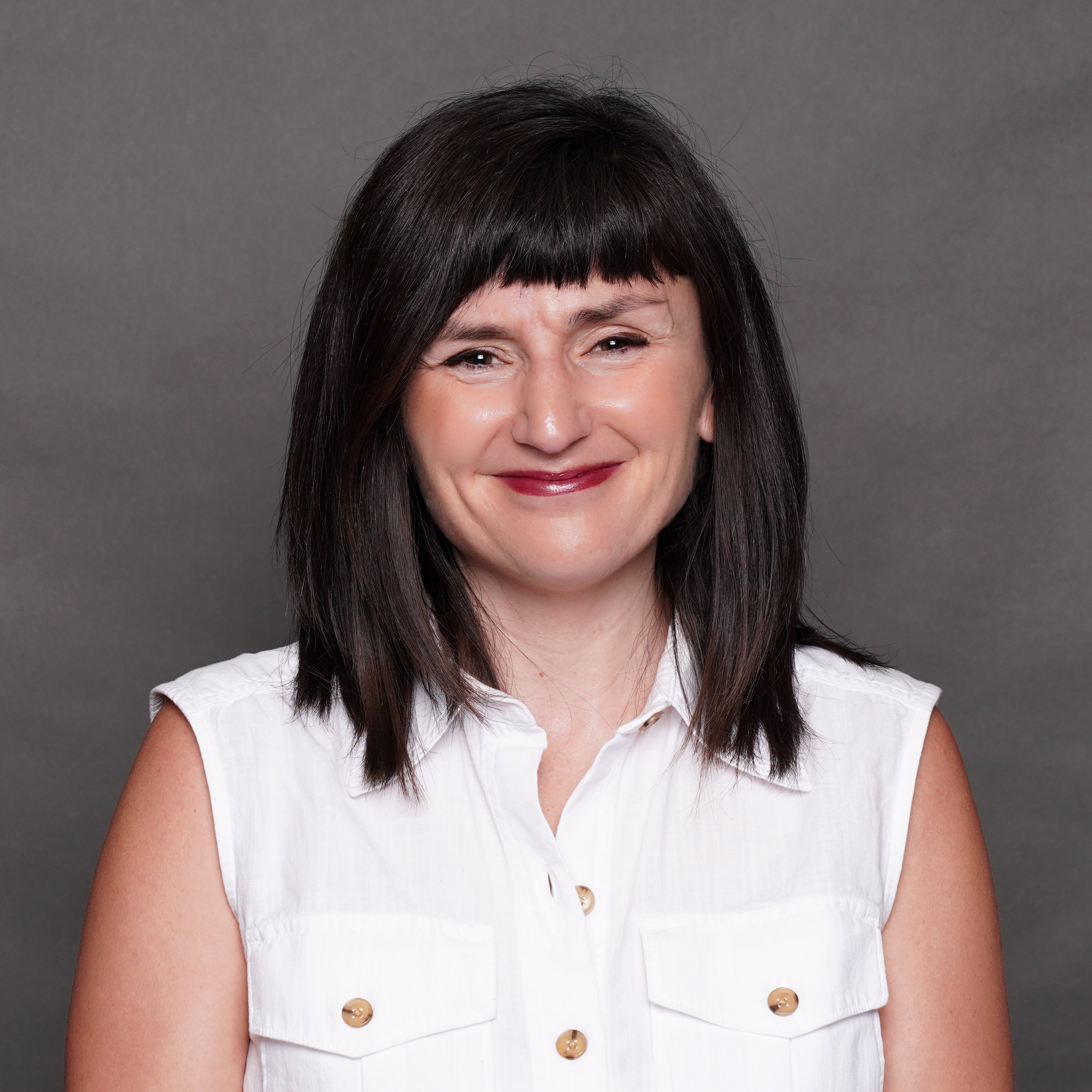 A woman's headshot smiling to camera wearing a white shirt.