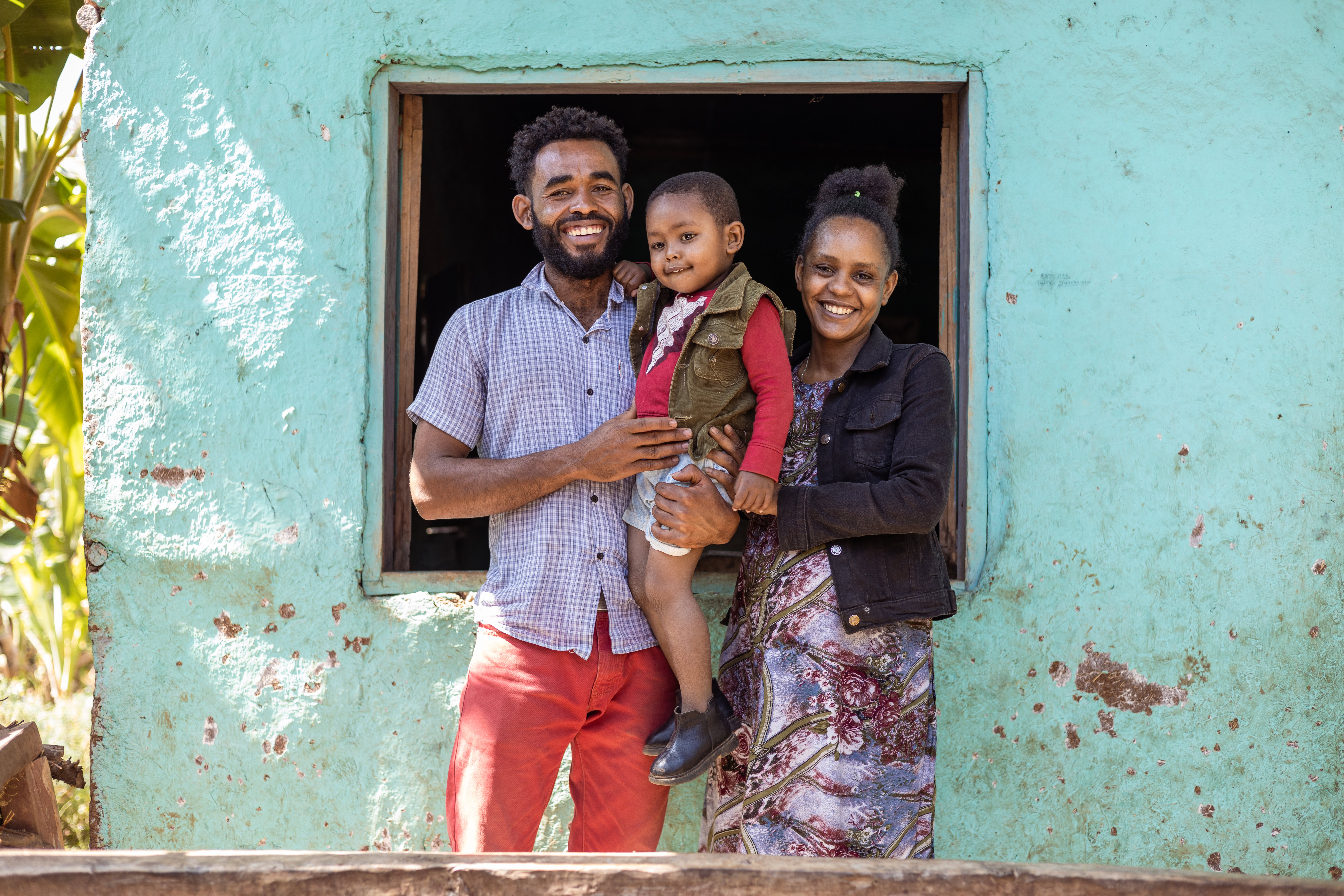 A child sits between their mom and dad inside their home in Ethiopia.