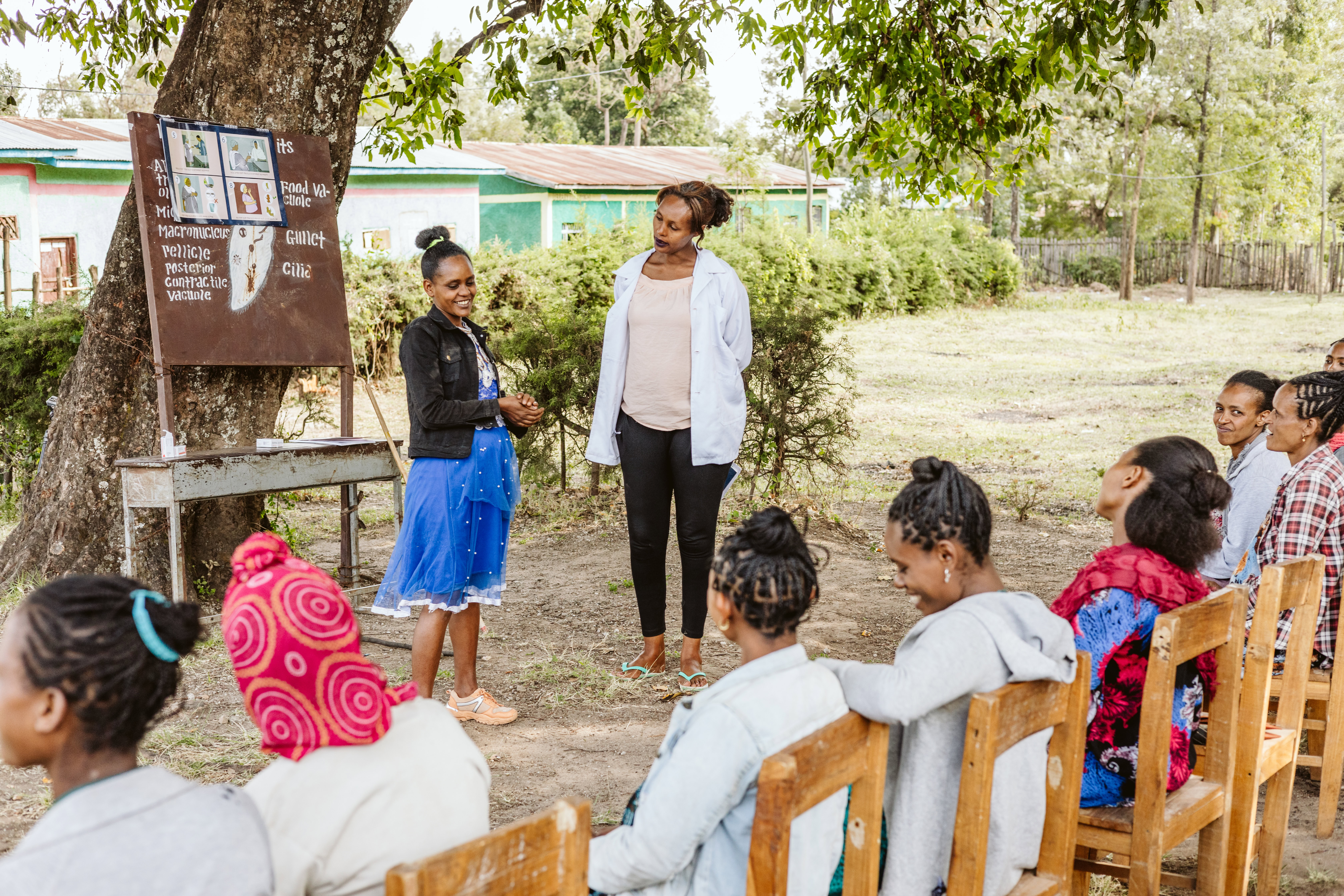 A pregnant woman and midwife in front of a crowd of pregnant women seated outside during a pregnant women's conference in Ethiopia. 