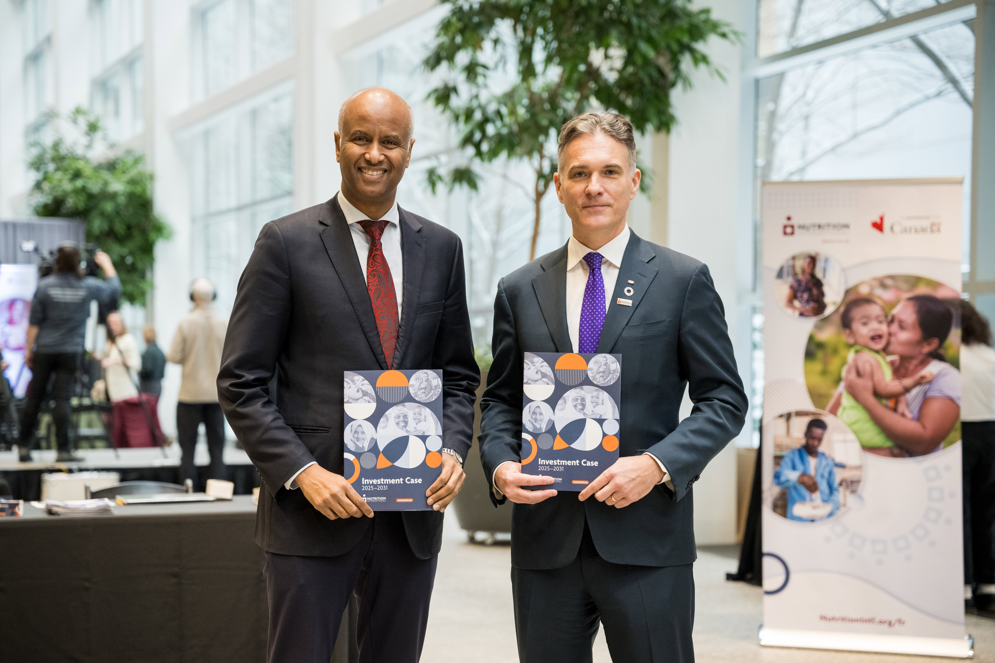 Two men holding brochures face the camera