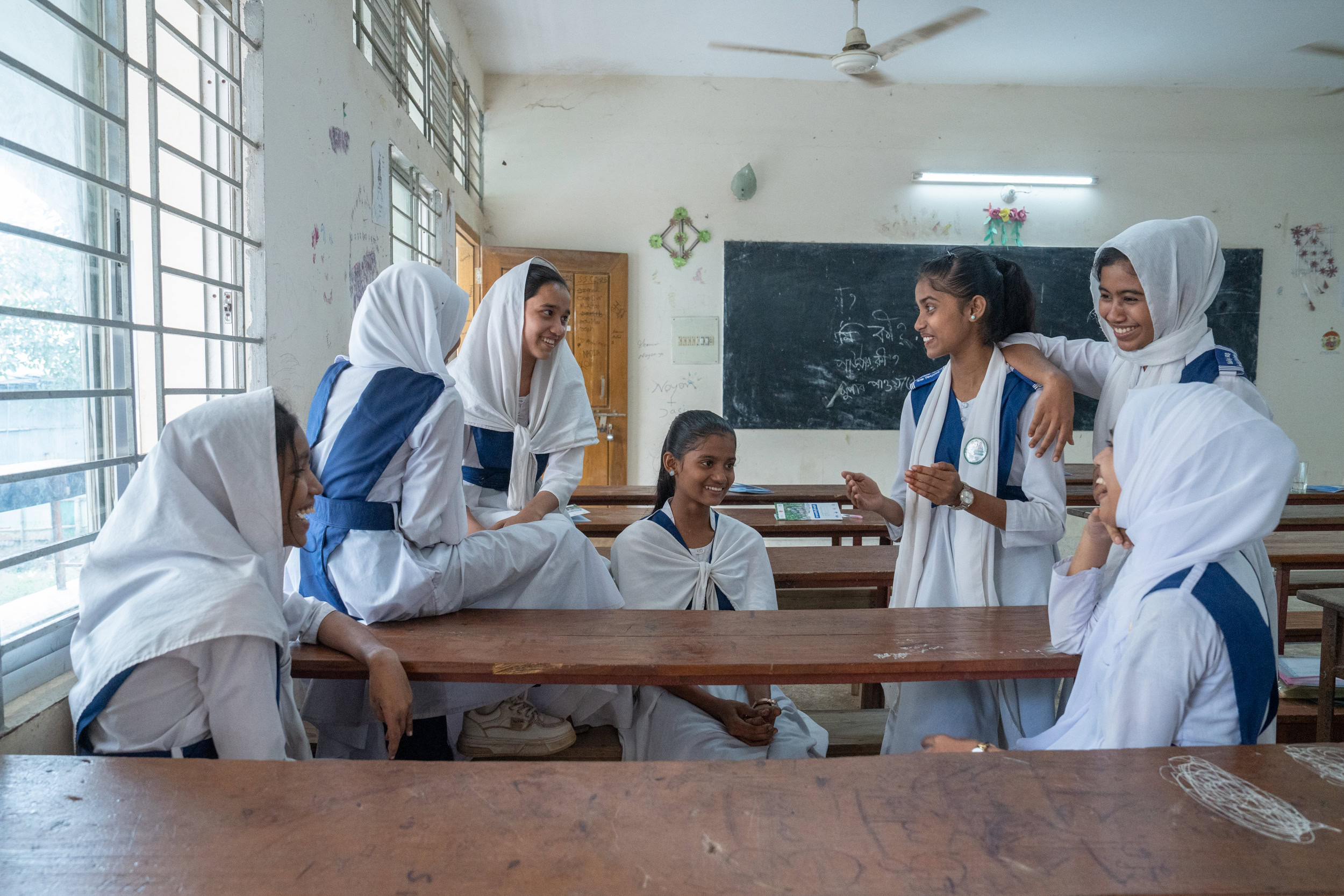 A group of girls chat and laugh in a clasroom.