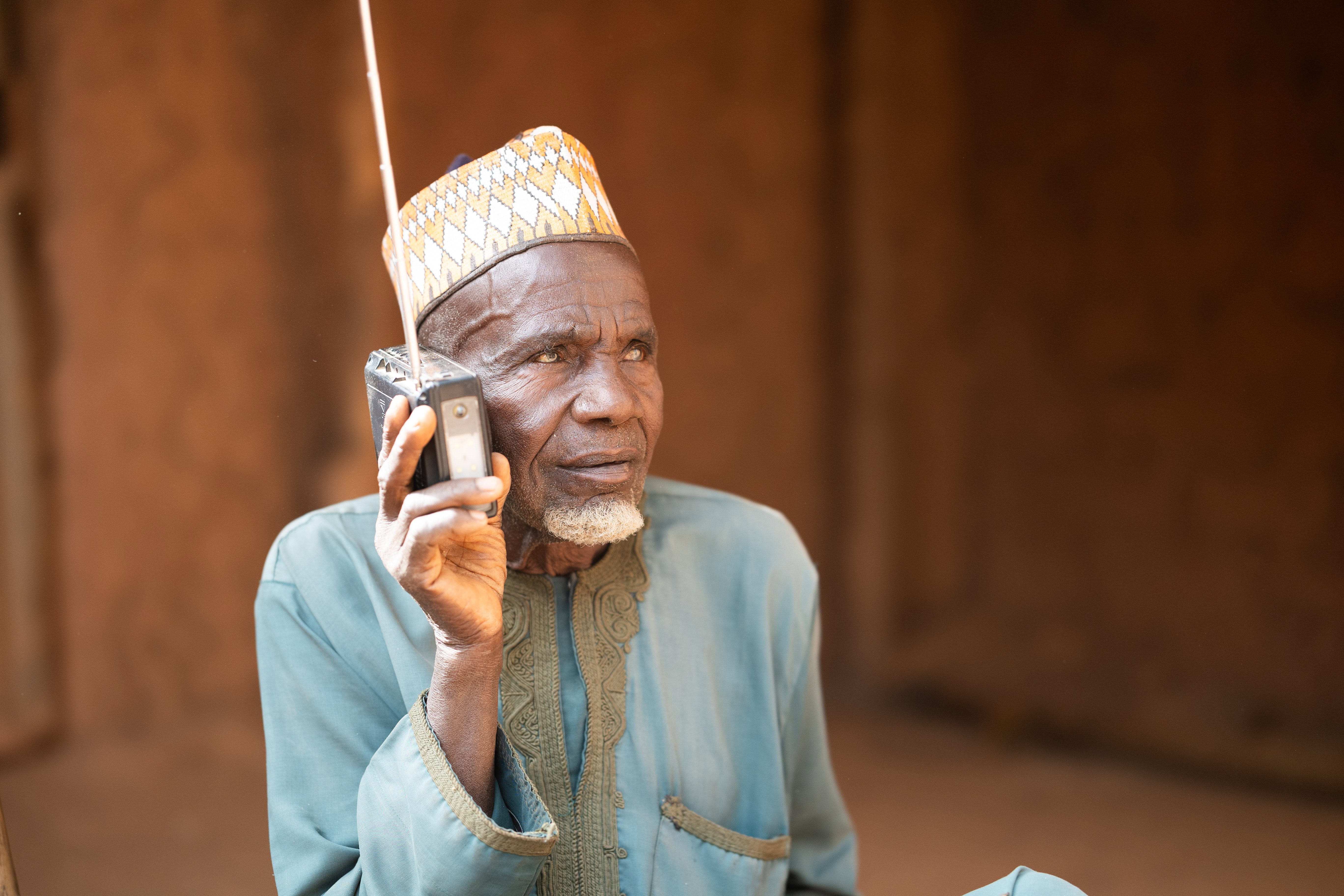 A man sits outside and listens attentively to a radio held up to his ear.