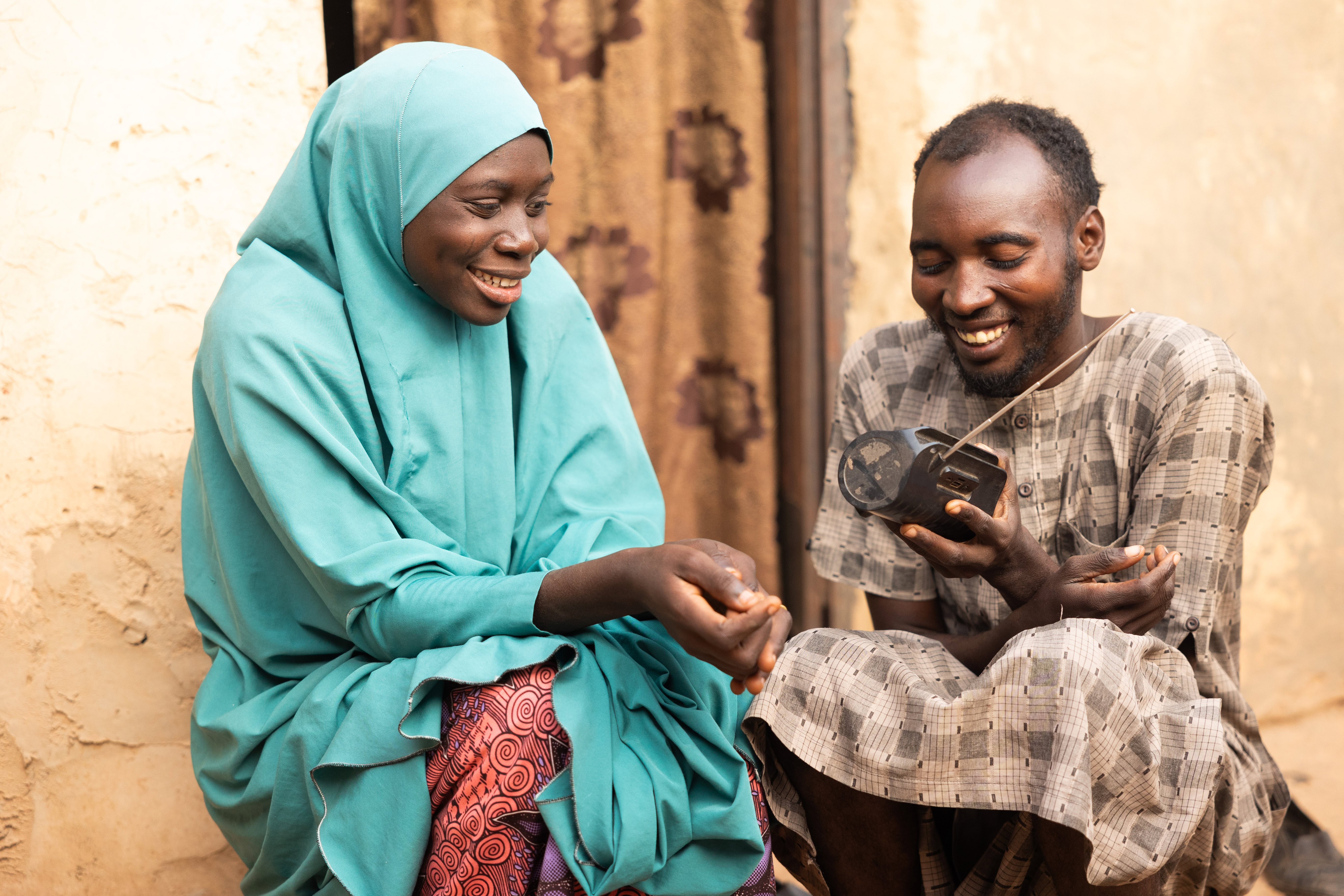 A woman and man sit outside on the stoop of their house laughing.