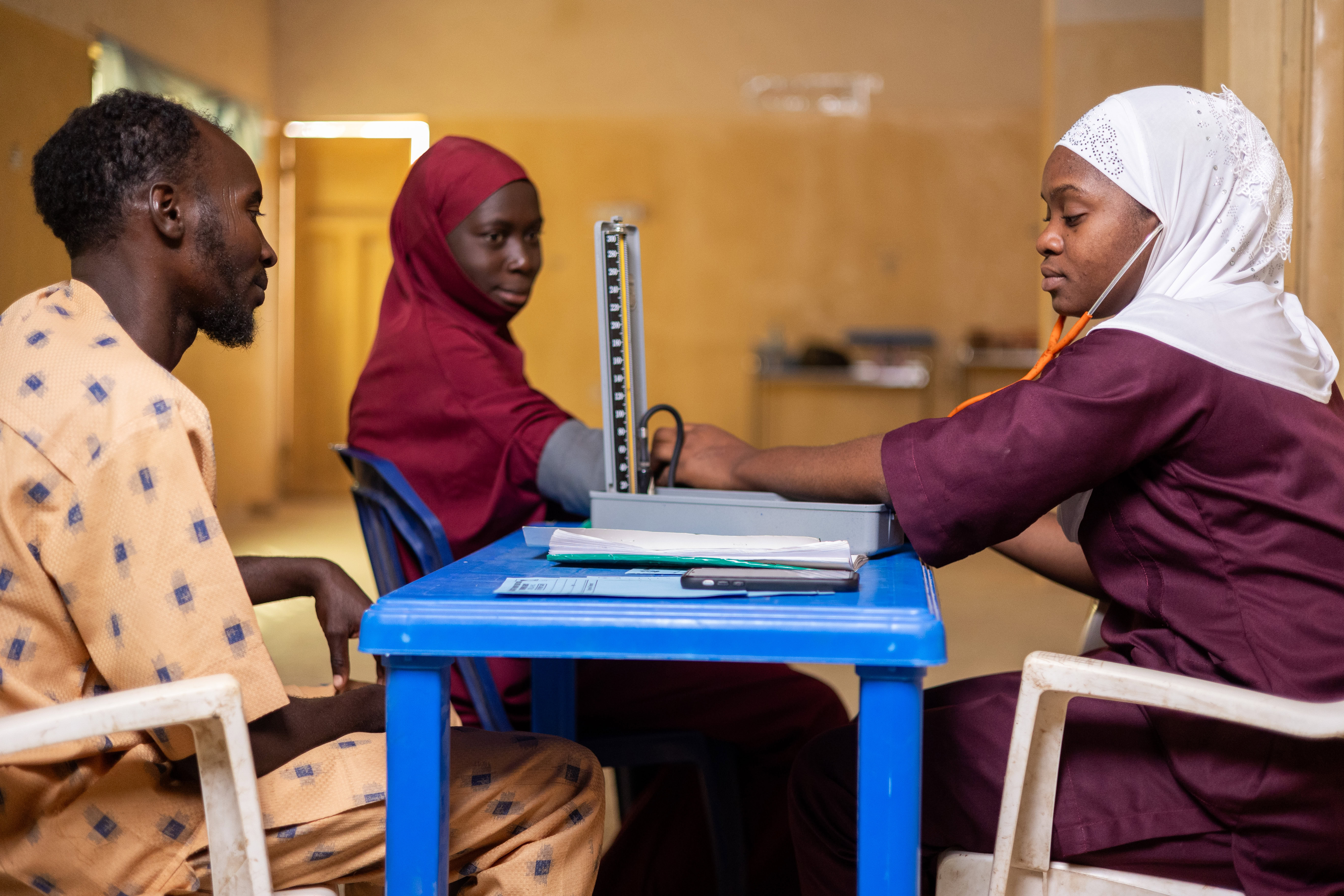 A husband and wife attend an antenatal care check up at a clinic in Northern Nigeria. They are seen by a midwife who is taking the women's blood pressure.
