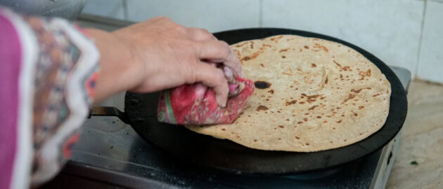 A hand is seen holding down chapatti on a pan as it is cooked.