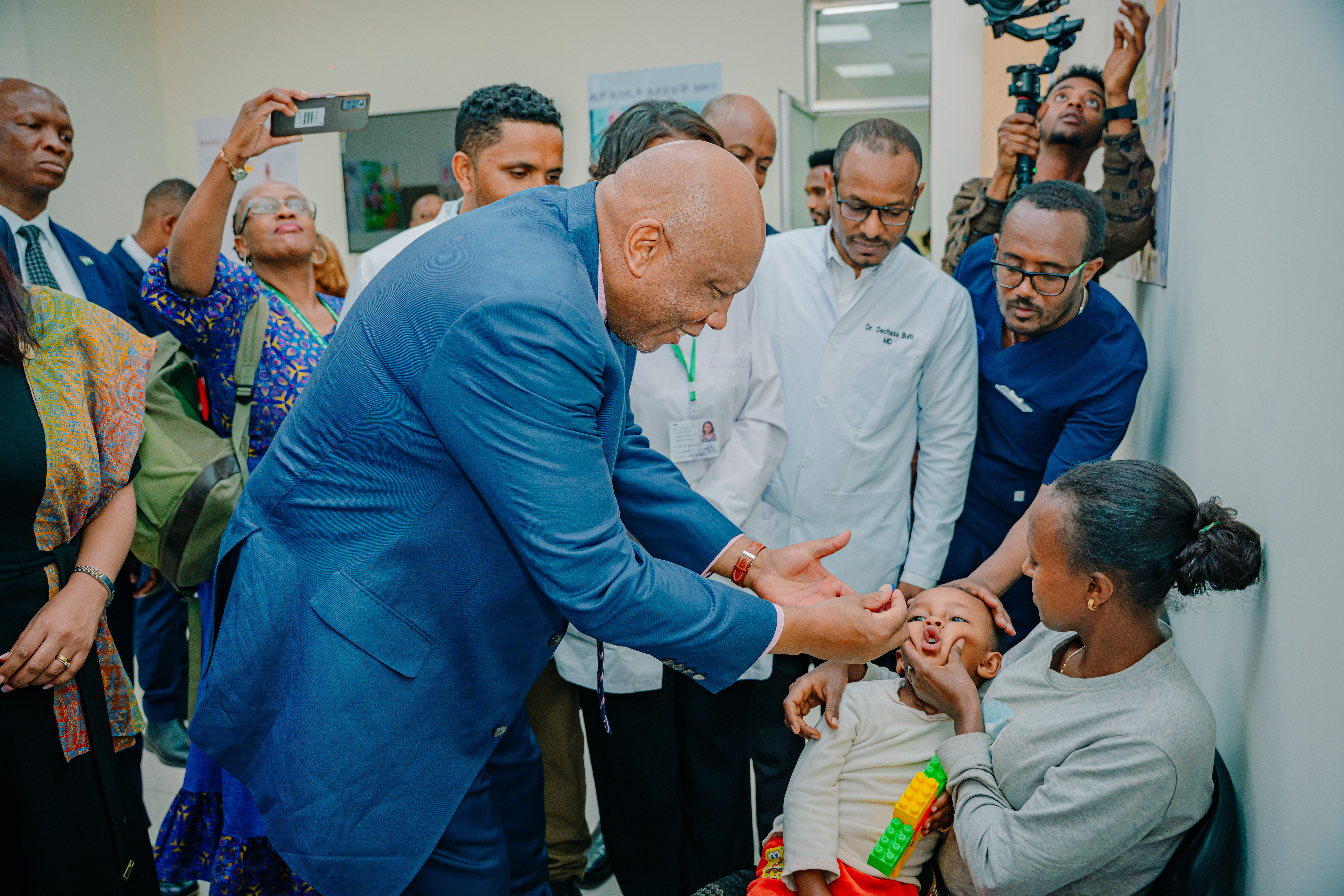 A man administers a vitamin A capsule to a child in its mother's arms