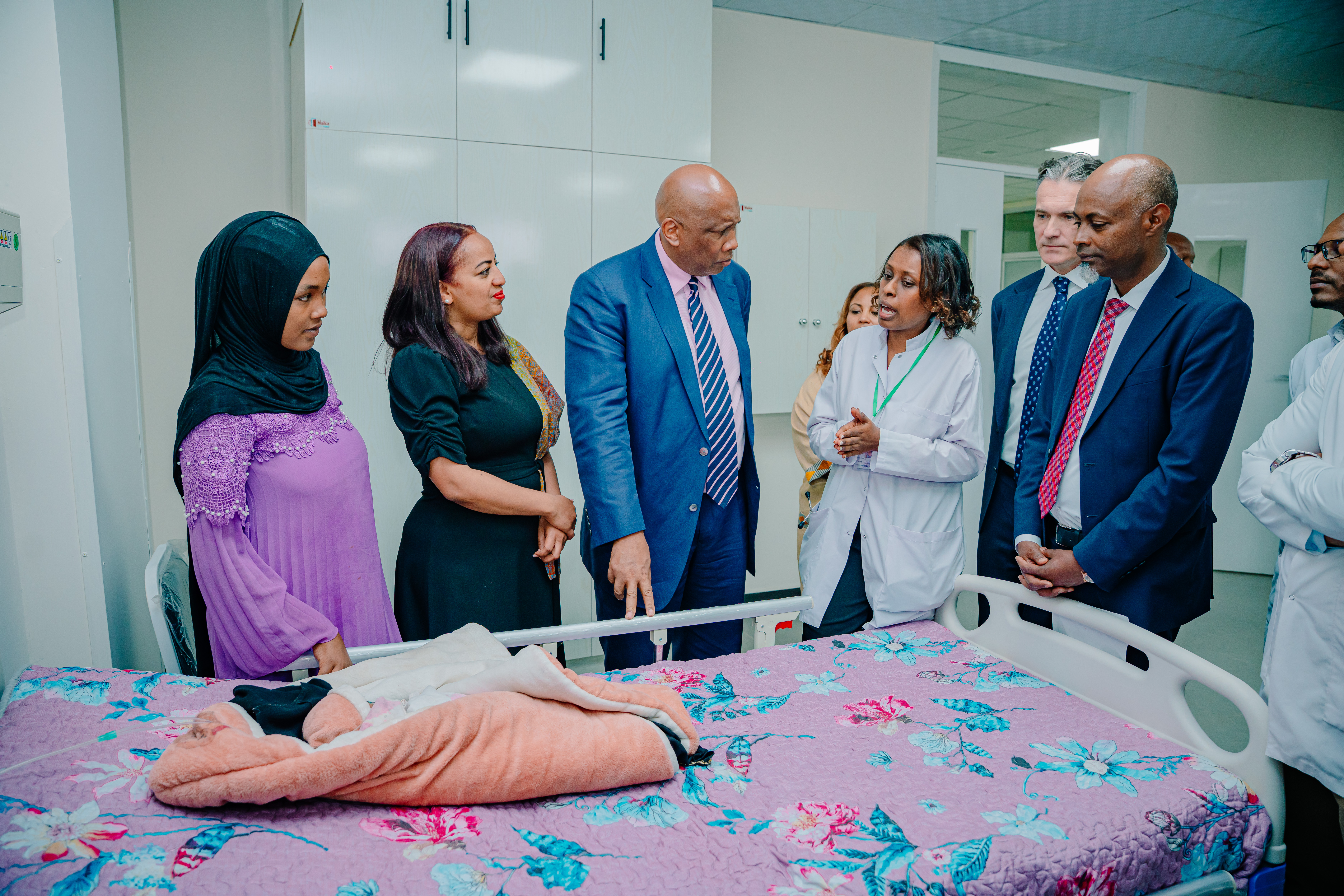 A group of men and women stand in front of a hospital bed talking to a doctor