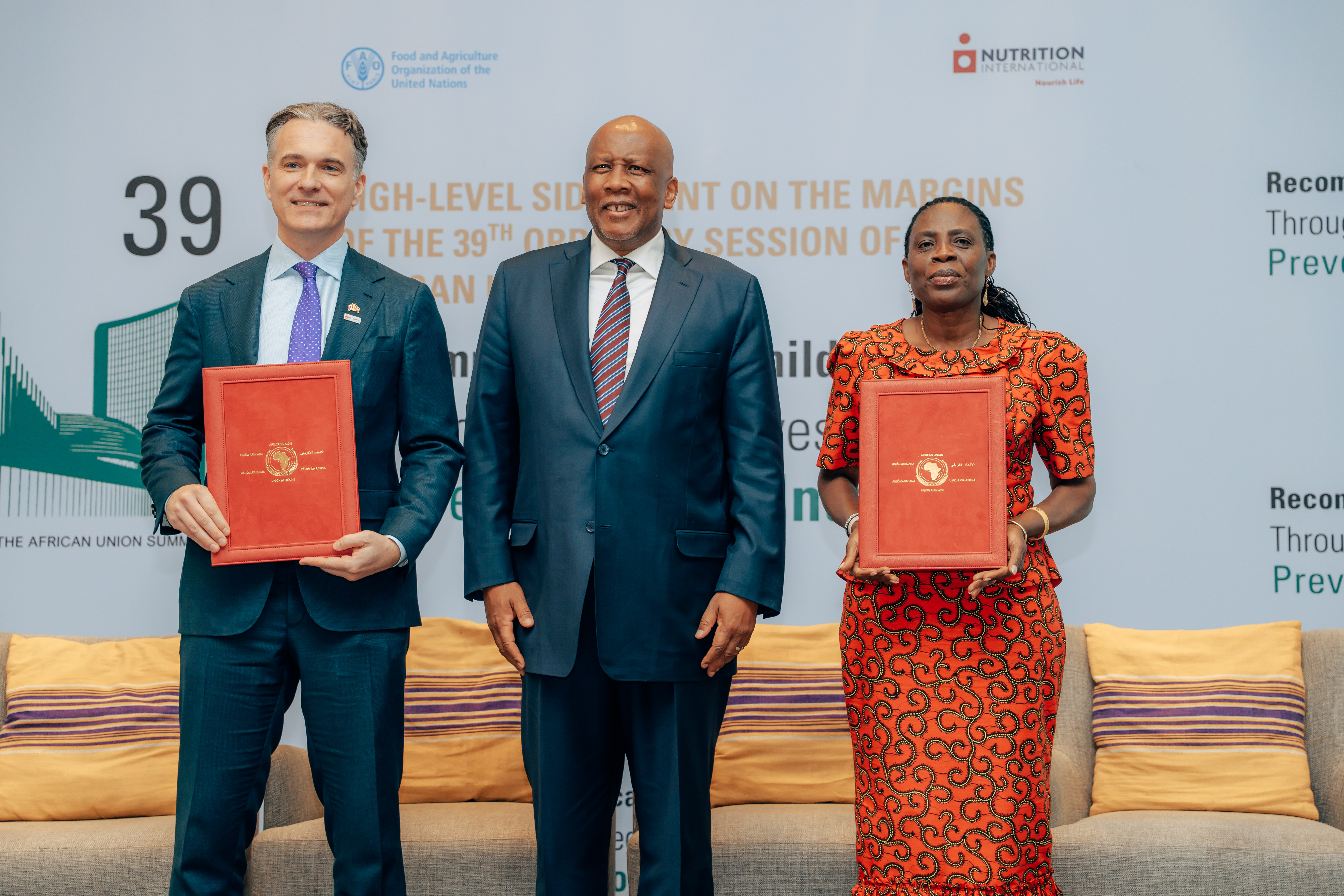 Two men and a woman stand smiling holding a red folder