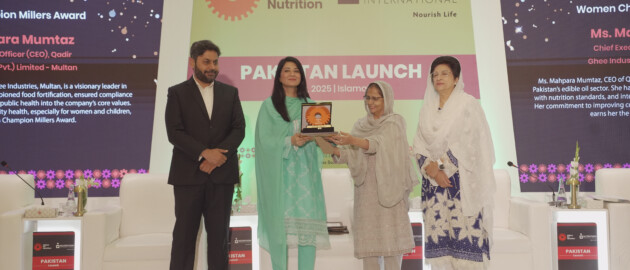 A woman accepts an award at the Pakistan Miller's Association for practices in food fortifcation. She is on stage with three other people.