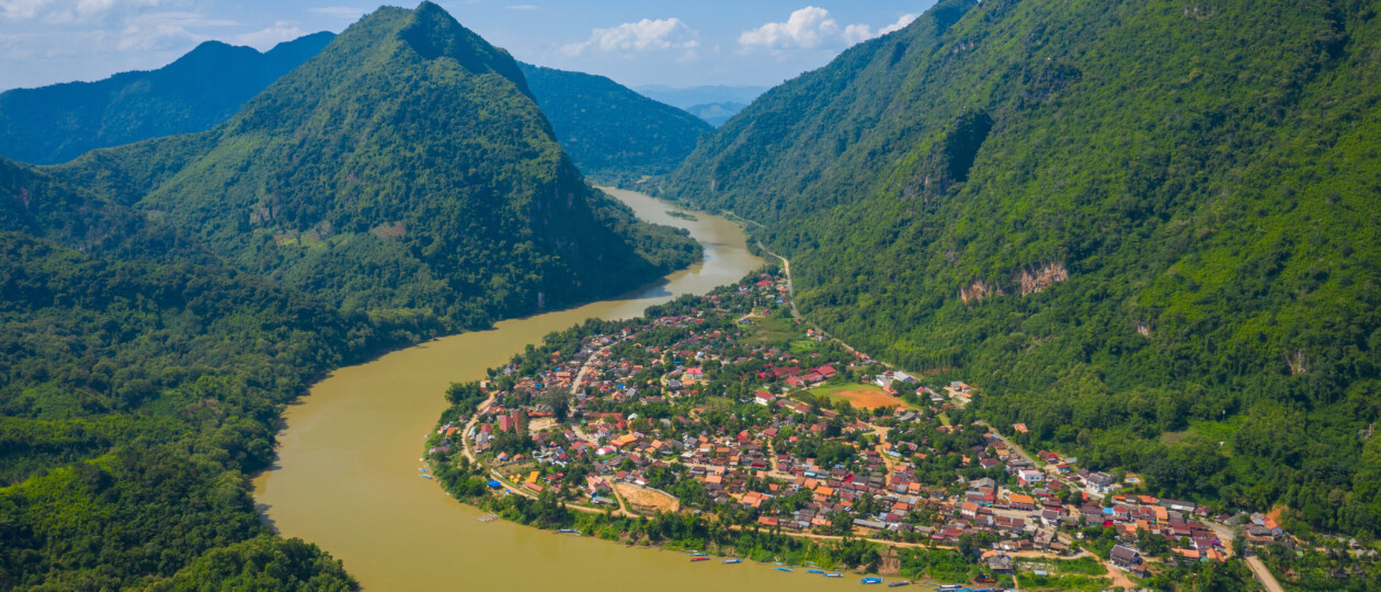 Aerial view of a village sitting on a winding river in a mountain landscape.