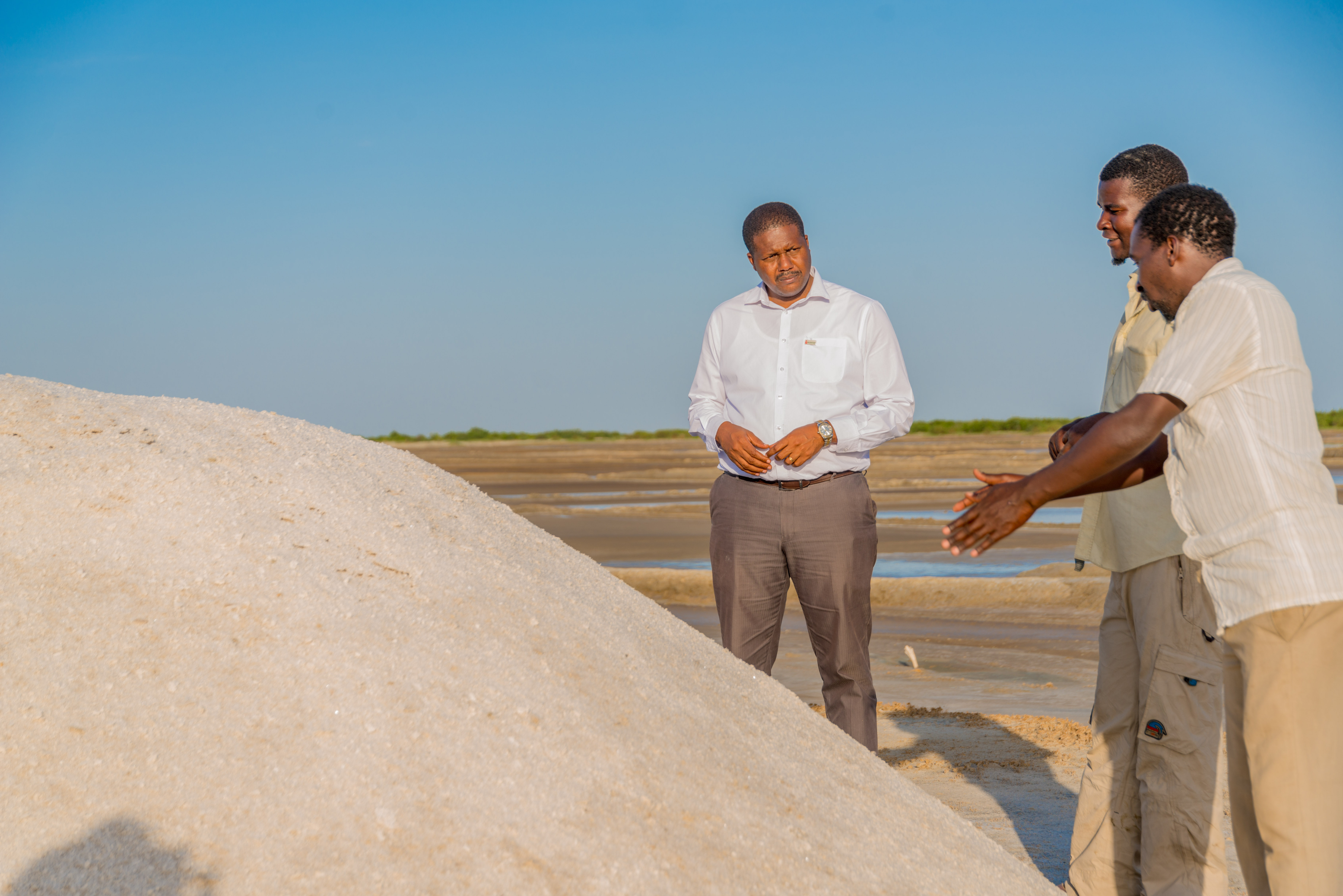 Men stand beside a mound of salt in an outside field.