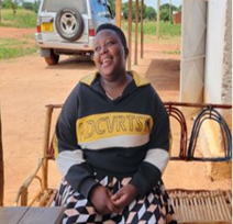 Smiling young woman sitting on a wooden bench outdoors, wearing a black/gray hoodie with yellow lettering and a checkered skirt.